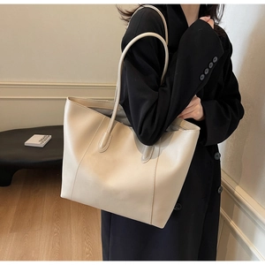 Detailed view of beige leather tote bag styled with a black coat for commute