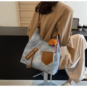 Detail of blue hobo canvas bag with brown leather trim and puppy charm on model