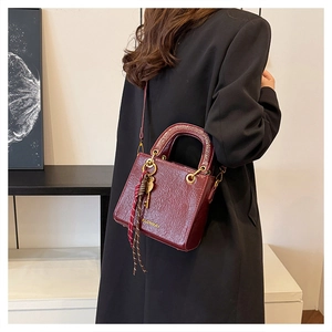 Detail of burgundy textured leather handbag with gold hardware and logo on black coat