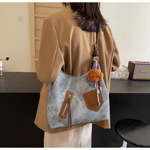 Detail of vintage grey washed tote with brown leather trim and a plush teddy bear charm