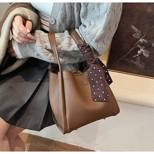 Close-up of brown pebbled leather bucket bag with decorative polka dot silk scarf handle