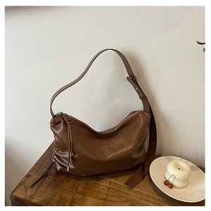 Detail view of brown leather hobo bag with tassel and knot on a wooden surface