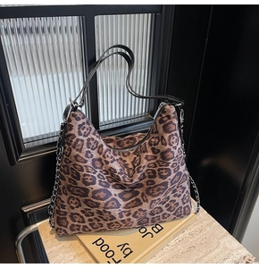 Detail of leopard print tote bag featuring black leather handles and silver chain strap