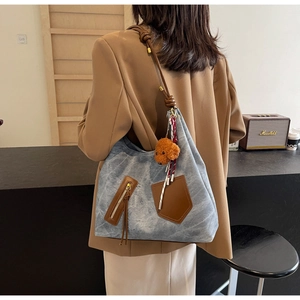 Detail of light blue denim tote bag with brown leather straps and plush poodle charm