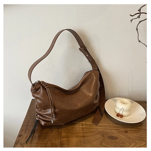 Detail of a brown leather hobo bag with adjustable strap and drawstring on wood table