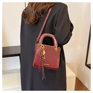 Detail of burgundy textured leather bag with gold hardware worn by model in black blazer