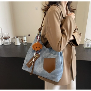 Detail of blue denim tote bag with leather trim and brown teddy bear plush charm