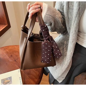 Close-up of brown bucket bag with lychee texture and polka dot silk scarf on handle