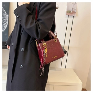 Detail of burgundy textured square bag featuring gold hardware and logo on a black suit