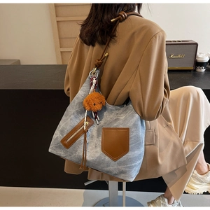 Detail of vintage denim crossbody bag with brown leather accents and a cute plush puppy charm