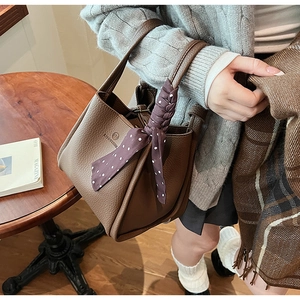 Detail of dark brown pebble leather bucket bag with purple polka dot scarf on handle