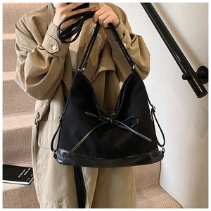 Large black canvas tote bag with leather bottom and decorative bow tie on front