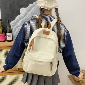 Detail of minimalist cream student backpack featuring brown leather logo and zipper pulls