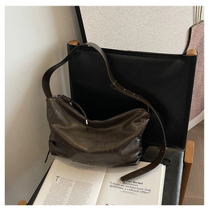 Detail of a large dark coffee hobo bag in vintage leather on a black chair with magazine