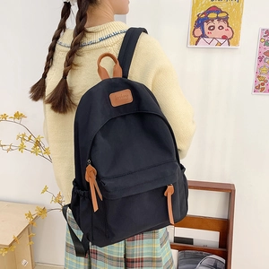 Detail of black nylon school backpack with leather handles shown in a lifestyle setting
