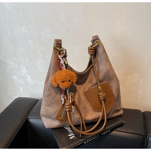 Close-up of vintage brown tote bag with leather pockets and orange plush pendant
