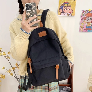 Detail of a black canvas backpack with a leather logo patch and front zipper pocket