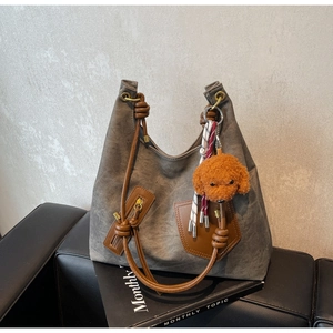 Detail of grey canvas tote bag with brown leather accents and plush teddy charm
