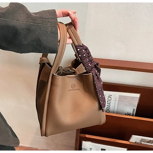Brown lychee leather bucket bag with top handles and a polka dot decorative scarf
