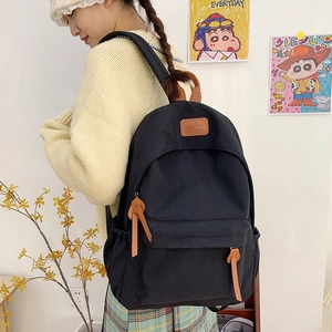 Detail view of the black school backpack featuring brown leather handle and zip pulls