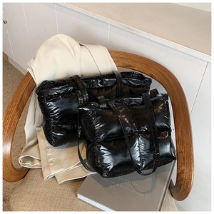 Detail view of glossy black quilted tote bags in two sizes on a stylish wooden chair