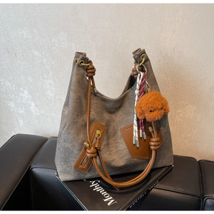 Detail of taupe tote bag with brown leather handles, zipper pocket and teddy bear charm
