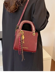 Deep red square handbag for women with gold logo and heart charm on black coat