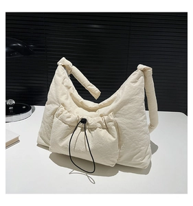 Detail of off-white padded nylon shoulder bag with drawstring pocket on a white table