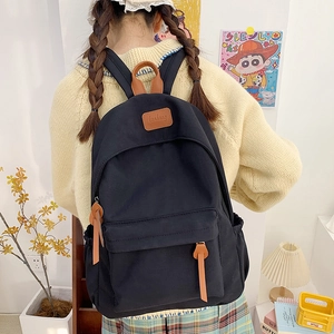 Detail of black canvas backpack showing brown leather logo and zipper accents