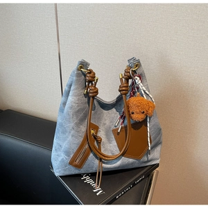 Detail of blue denim hobo bag with brown leather handles and teddy bear pendant charm