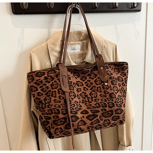Leopard print canvas tote bag with brown leather handles hung over a khaki trench coat