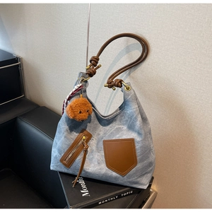 Detail of blue canvas hobo bag with leather straps, plaid scarf, and teddy charm
