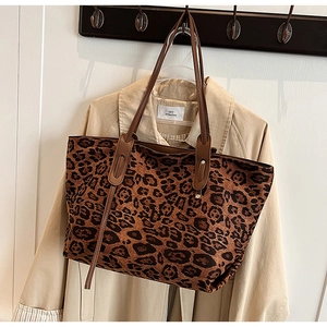 Detail of leopard print tote bag with brown leather straps hanging on a beige coat
