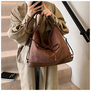 Brown matte suede tote bag with bow detail shown by a model in a trench coat