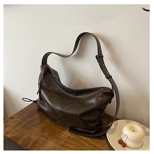 Detail of a vintage dark brown hobo shoulder bag with a metal zipper on a wooden table