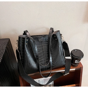 Close-up of black crocodile pattern tote bag with wide woven strap on a wooden rack