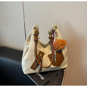 Detail of canvas tote bag with brown leather handles and plush dog charm accessory