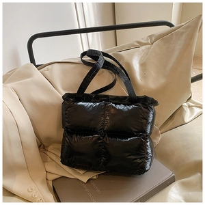Close-up of black quilted puffer tote bag with glossy finish on a stylish book