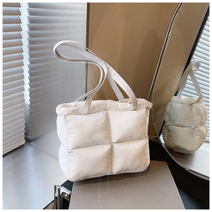 Detail of a white quilted puffer tote bag with stitched texture on a neutral surface