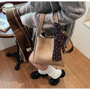 Detail of khaki lychee grain leather bucket bag with logo and decorative polka dot scarf