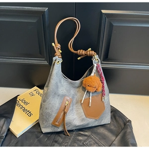 Detail of grey retro tote bag with brown leather straps and plush puppy charm