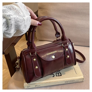 Detail of burgundy Boston bag showing gold hardware and embossed fashion logo lettering
