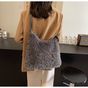 Detail of grey plush shoulder bag with smooth leather strap shown in a cozy interior setting
