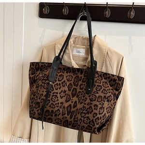 Detail of leopard print tote bag with black leather straps hanging on a khaki trench coat
