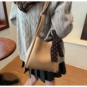 Detail of light coffee bucket bag with lychee texture and decorative silk scarf accessory