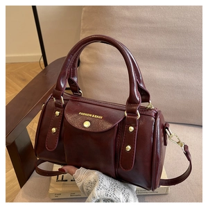 Detail view of burgundy Boston bag with gold rivets and dual handles on a sofa