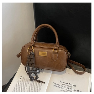 Dettaglio della borsa Boston marrone vintage con texture in pelle, targa dorata e ciondolo gatto