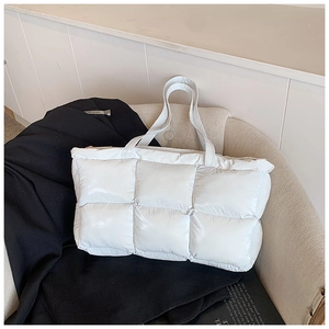 Close-up of white quilted puffer tote bag with glossy finish on a cream sofa