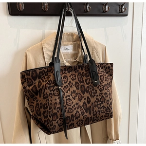 Close-up of leopard print tote bag with black leather straps hanging on a wooden rack