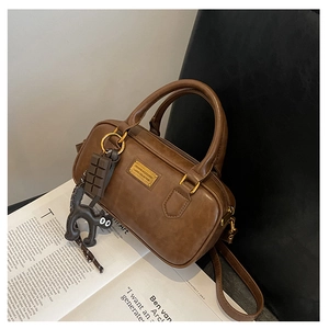 Dettaglio borsa Boston marrone vintage con ciondoli a gatto e targhetta dorata